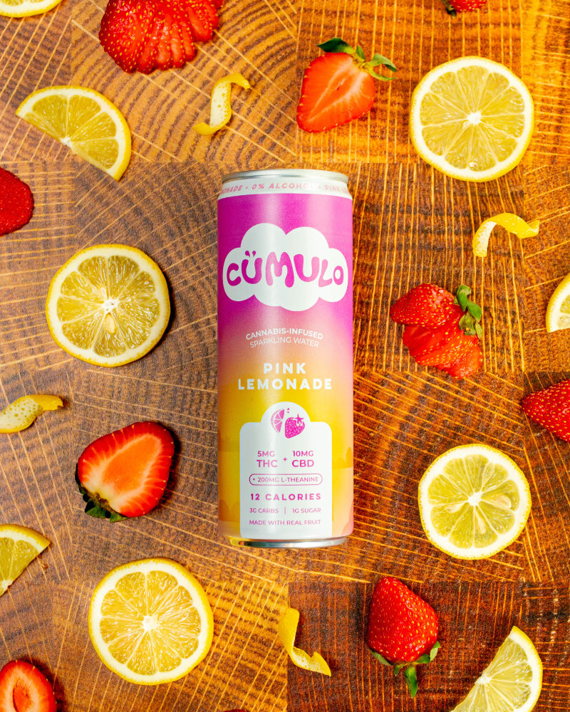 Cumulo Pink Lemonade can on a wooden surface with lemons and strawberries.